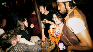 A group of people socializing and enjoying drinks around a small table at a dimly lit bar.
