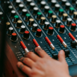 A hand adjusts sliders and knobs on an AI-powered audio mixing console, with various controls and colored buttons visible.