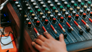 A hand adjusts sliders and knobs on an AI-powered audio mixing console, with various controls and colored buttons visible.