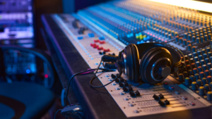 A pair of headphones rests on a large audio mixing console with numerous buttons, knobs, and faders in a recording studio, where sound engineers skillfully manage audio data for perfect recordings.