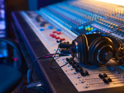 A pair of headphones rests on a large audio mixing console with numerous buttons, knobs, and faders in a recording studio, where sound engineers skillfully manage audio data for perfect recordings.