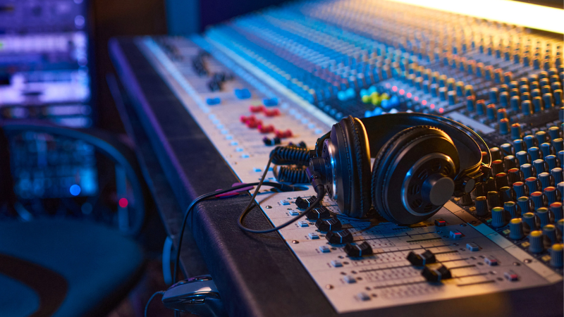 A pair of headphones rests on a large audio mixing console with numerous buttons, knobs, and faders in a recording studio, where sound engineers skillfully manage audio data for perfect recordings.