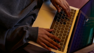 Close-up of a person wearing a grey sweatshirt typing on a laptop keyboard, possibly researching the best email newsletter platforms for musicians.