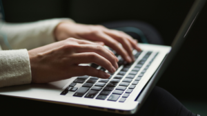 Close-up of a person typing on a laptop keyboard, their hands moving in a symphonic rhythm, with the screen partially visible in the background.