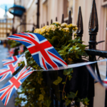 Union Jack flags are strung along a black iron fence decorated with plants and flowers on a city street, adding festive flair as London prepares for SXSW London 2026.