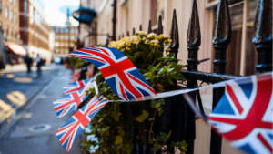 Union Jack flags are strung along a black iron fence decorated with plants and flowers on a city street, adding festive flair as London prepares for SXSW London 2026.