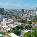 Aerial view of a modern cityscape with tall buildings, busy streets, and scattered greenery under a partly cloudy sky, near the Congreso Músicapress center.