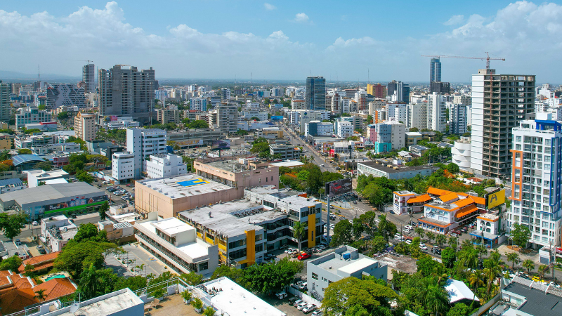 Aerial view of a modern cityscape with tall buildings, busy streets, and scattered greenery under a partly cloudy sky, near the Congreso Músicapress center.