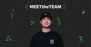 A team member in a black cap and black "SYMPHONIC" shirt stands in front of a grid background with the text "MEET the TEAM" and green graphic elements.
