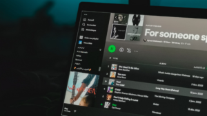 A laptop screen displays the Spotify app with a playlist open, showcasing song titles and album covers—perfect for playlist pitching—against a dark, blurred background.