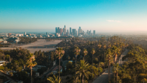 Aerial view of downtown Los Angeles skyline with palm trees in the foreground on a clear, sunny day, capturing the vibrant city energy during the GMS State of Music in Media Conference.